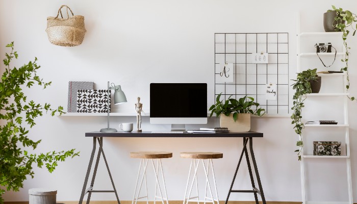 In a small modern home office room there is a computer on table with chairs